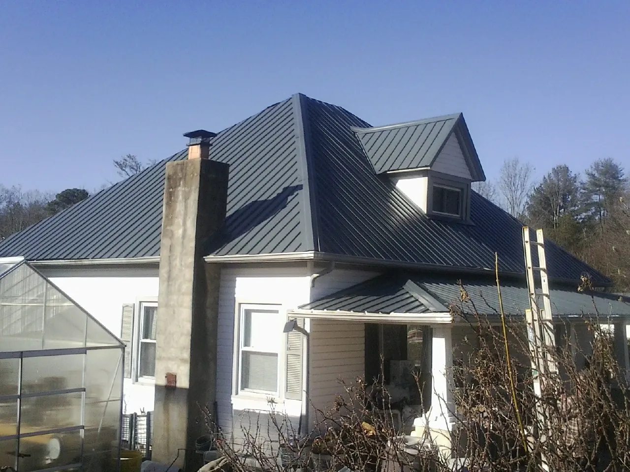 Dark blue standing seam metal roof on a white farmhouse with dormer — Slate & Tile Roof Repair by Roofing Brothers in Anza