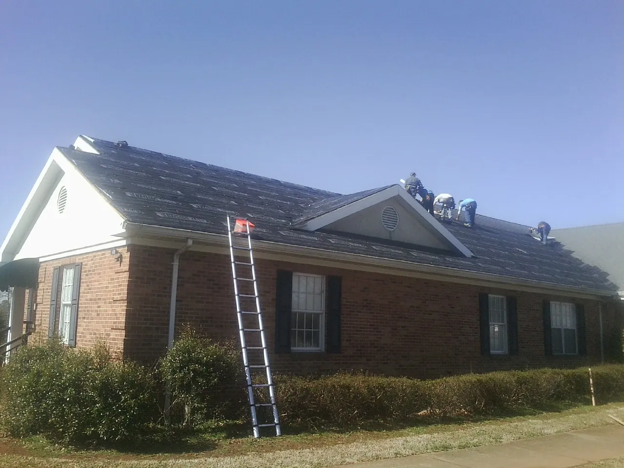 Crew tearing shingles off a brick ranch roof with a ladder set — Emergency Roof Repair work by our crew in Anza