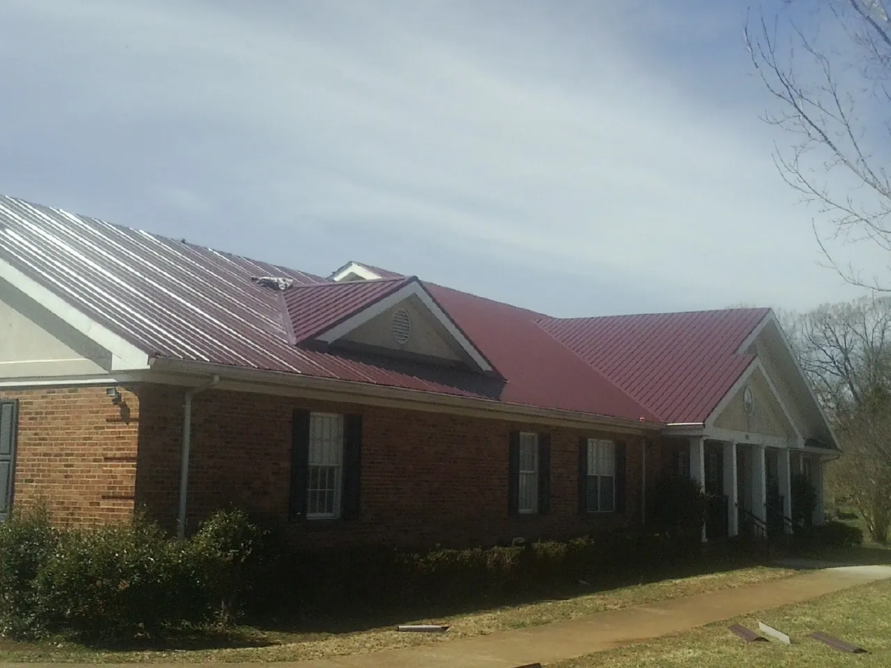 Red metal roof with gabled entries on a long brick building, from a Hail Damage Roof Repair job in Anza