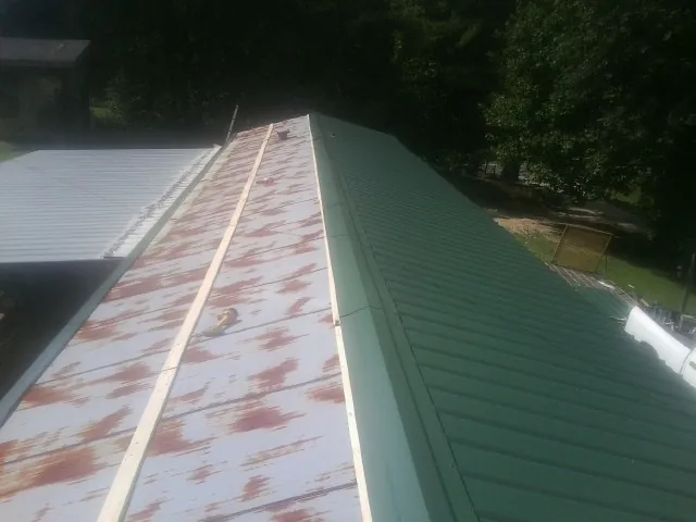 Old rusted panels beside newly installed green metal roofing — Wind Damage Roof Repair by Roofing Brothers in Anza