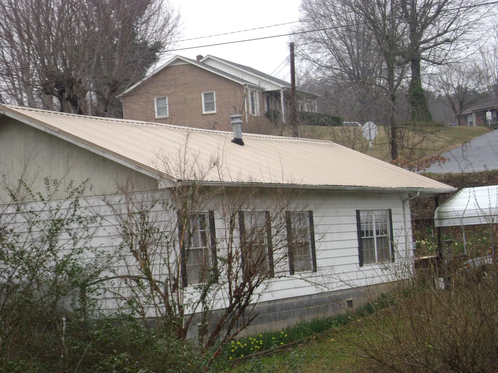 Tan metal roof on a white sided house set into a hillside — Commercial Roofing by Roofing Brothers in Anza